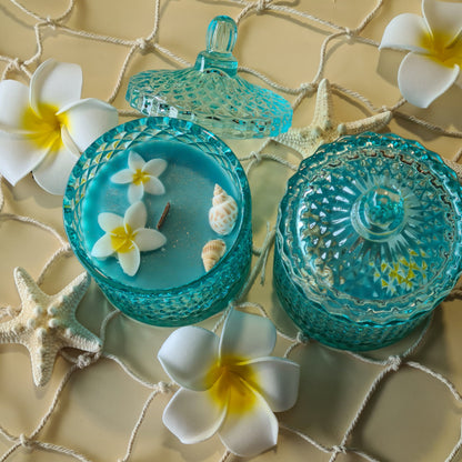 geurkaars bue lagoon, voorzien van een houten wiek, in een azuur blauw glas met sierlijk deksel, geur kaars is golden sands, versierd met echte schelpen, zomerkaars